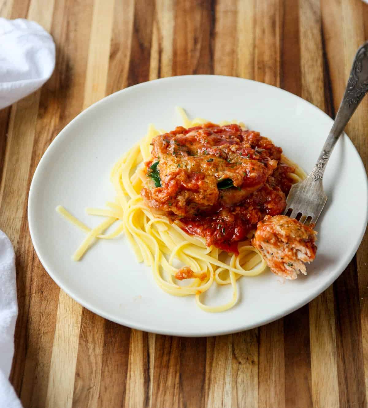 Chicken and pasta on a white plate with a fork on a wooden board.