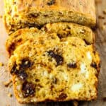 A loaf of sun-dried tomato bread with two slices cut.