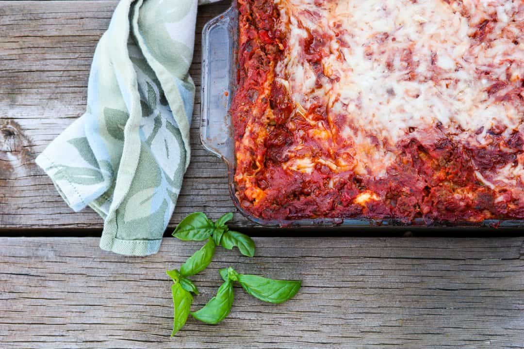 A pan of baked lasagna sitting on top of a wooden cutting board
