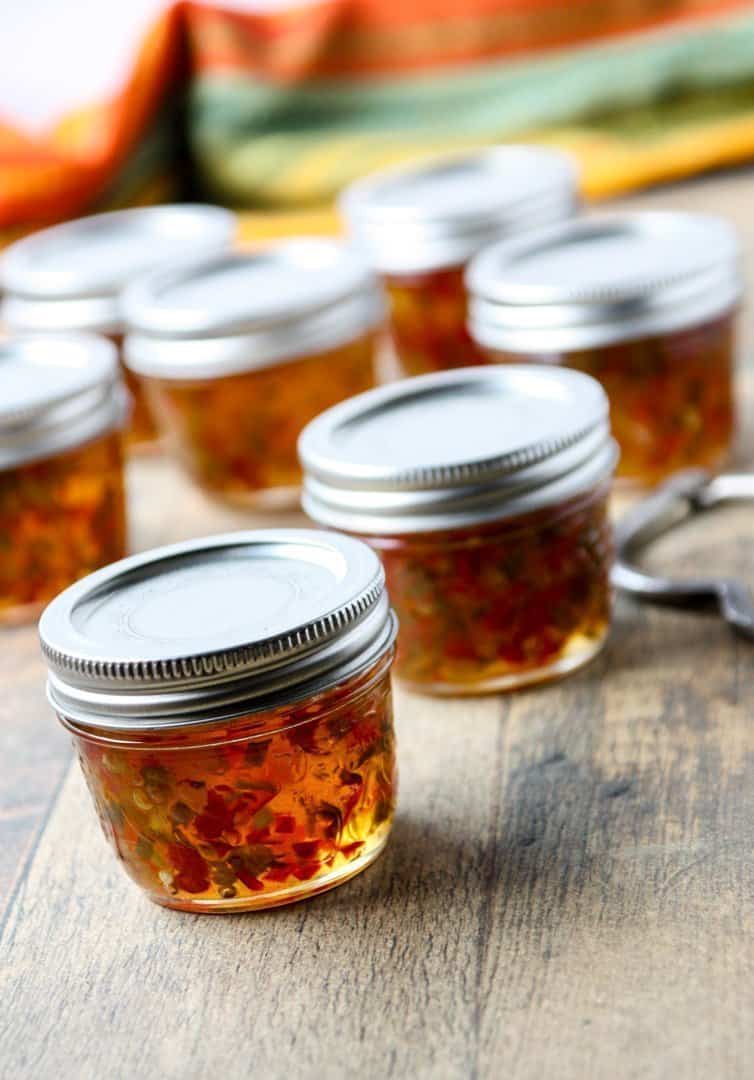 Jars of homemade pepper jelly on a wooden countertop.