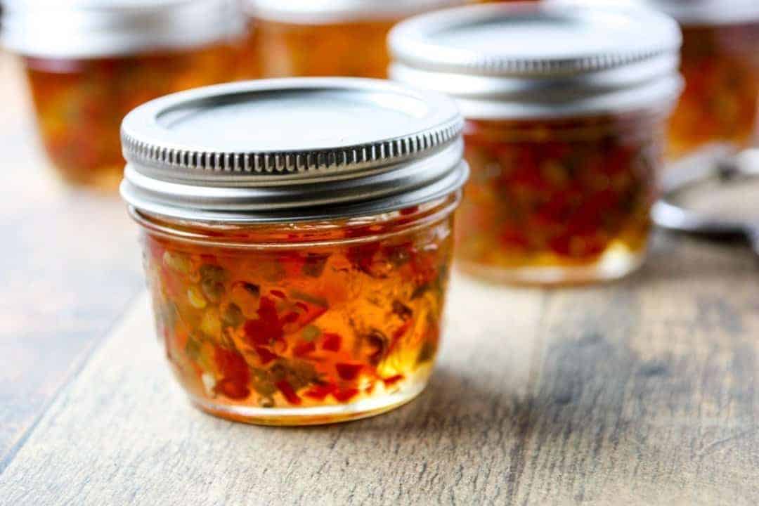 A close up of a jar of pepper jelly on a wooden countertop.