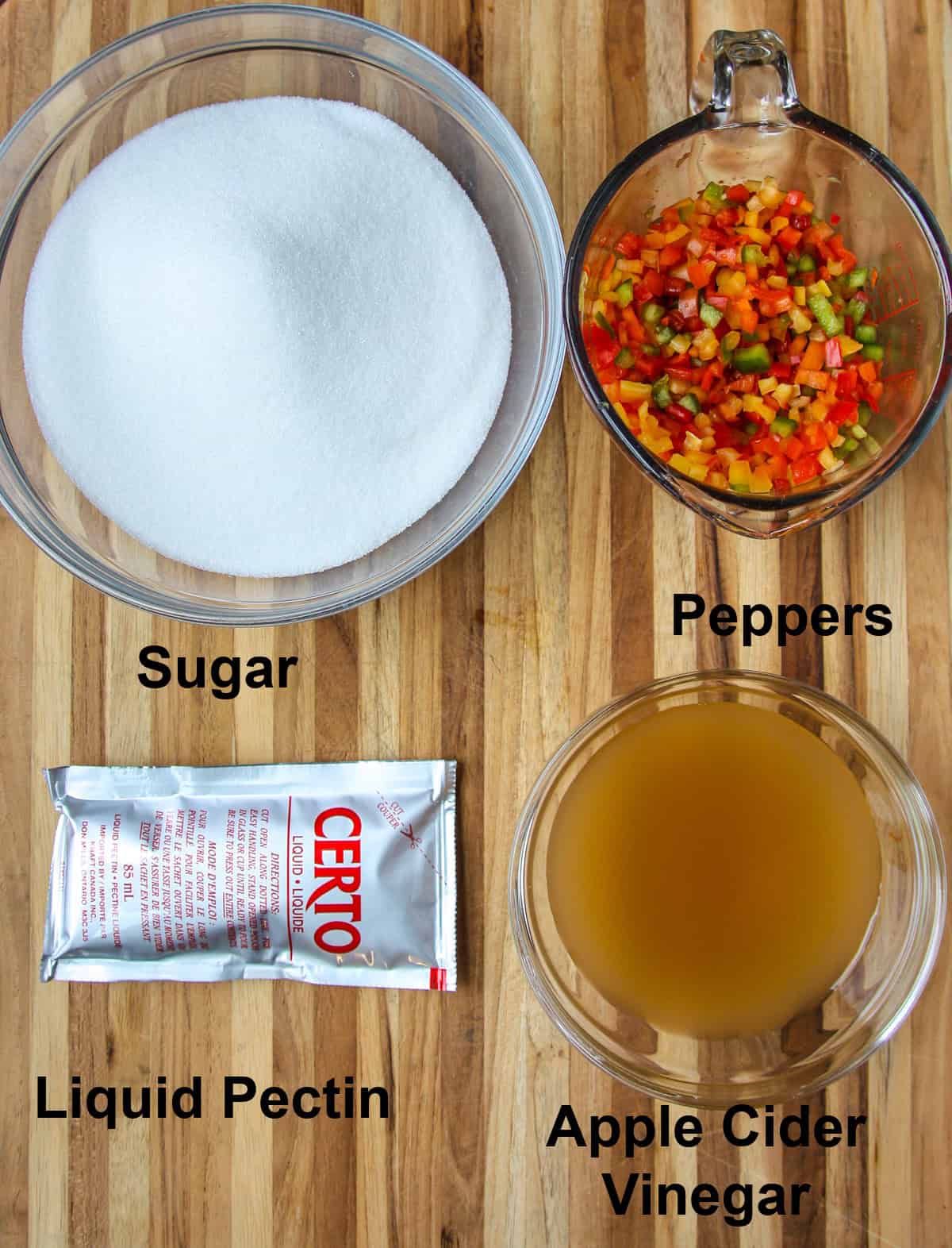 The ingredients for making pepper jelly in glass bowls on a wooden board.