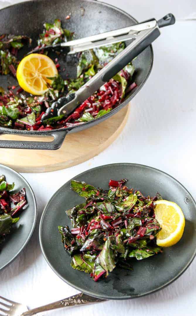 Two plates of cooked beet tops with a lemon wedge