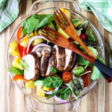 Salad in a glass bowl topped with sliced jerk chicken breast.