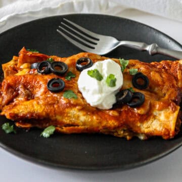 Two leftover turkey enchiladas on a black plate with a silver fork